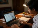 Ilustrasi seorang anak sedang fokus mengerjakan tugas menggunakan laptop di kamarnya pada malam hari.